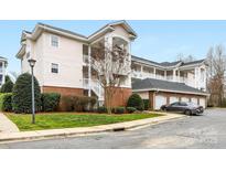 Condominium exterior featuring manicured lawn and landscaping, brick accents, covered balconies, and private garages at 8759 Coralbell Ln, Charlotte, NC 28213