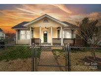 Charming home featuring a covered front porch with columns and a fenced yard under a vibrant sunset at 1111 W 4Th Ave, Gastonia, NC 28052