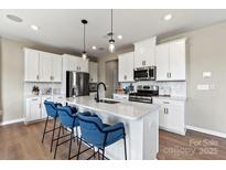 Bright kitchen features a center island with a sink, stainless steel appliances, white cabinets, and pendant lighting at 15212 Caspian Way, Charlotte, NC 28278