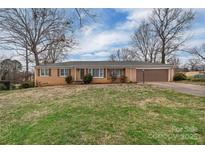 Charming brick ranch with a well-manicured lawn, mature trees, and attached garage at 107 Pinelake Dr, Kings Mountain, NC 28086