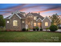Stunning brick home with turret, manicured lawn, and professional landscaping at sunset at 121 Dabbling Duck Cir, Mooresville, NC 28117
