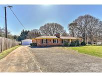 Charming brick ranch-style home with a detached garage, and spacious front yard on a sunny day at 1356 Ford Dr, Lowell, NC 28098