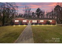 Charming brick ranch-style home with a walkway, illuminated by landscape lighting at dusk, and a well-manicured lawn at 407 Pinecroft Ln, Spencer, NC 28159