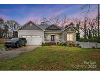 Charming home featuring stone accents, covered porch and two-car garage, set against a colorful evening sky at 125 Jefferson Dr, Locust, NC 28097