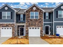 Charming townhouse featuring a stone facade, blue siding, and individual garages, set under a bright, cloudy sky at 522 Trading Post Ln, York, SC 29745