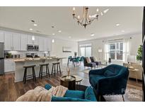 Bright, open-concept living room with wood floors and modern furnishings flowing into the kitchen and dining areas at 6450 Keeton Ln, Harrisburg, NC 28075