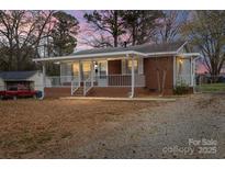 Charming single story home with brick and siding, a covered front porch, and mature trees at 208 Tomberlin Rd, Mount Holly, NC 28120