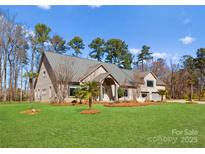 Expansive brick home featuring mature trees, a metal roof, and a well manicured lawn under a bright blue sky at 16455 Harbor View Rd, Charlotte, NC 28278