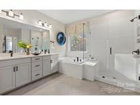 Bright bathroom with white cabinets, dual vanity, tub, and glass shower featuring black hardware and herringbone tile floors at 164 Holsworthy Dr, Mooresville, NC 28115