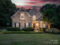 Charming two-story home with brick facade, manicured lawn, and mature landscaping with warm sunset lighting at 821 Lynnwood Farms Dr, Fort Mill, SC 29715