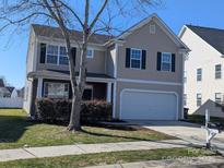 Tan two-story home featuring a two-car garage, black shutters, well-manicured lawn, and mature landscaping at 10943 Trout Creek Pl, Davidson, NC 28036