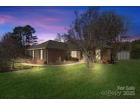 Charming brick home with well-manicured lawn and landscape lighting under colorful sky at 861 Emerson Dr, Mooresville, NC 28115