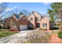 Stunning brick home featuring a well-manicured lawn, 3 car garage and lush landscaping against a bright blue sky at 4858 Sagittarius Cir, Denver, NC 28037