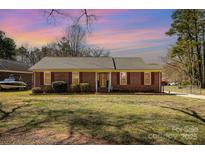 Charming single-story brick home with manicured lawn and mature trees, bathed in the warm glow of the setting sun at 11018 Despa Dr, Mint Hill, NC 28227