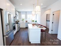 Bright kitchen features white cabinetry, stainless steel appliances, pendant lighting, and a spacious center island with seating at 317 Old Town Village Rd, Waxhaw, NC 28173