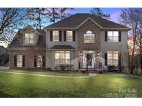 Charming two-story home featuring a brick facade, manicured lawn, and inviting entryway with red shutters and flower pots at 7510 Plumcrest Ln, Harrisburg, NC 28075