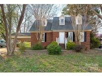 Charming brick home featuring dormer windows, a covered carport, and mature trees at 82 Paddington Sw Dr, Concord, NC 28025