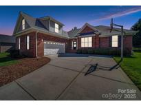 Brick home featuring a two-car garage, well-manicured lawn, and a long driveway at twilight at 108 Avaclaire Way, Indian Trail, NC 28079