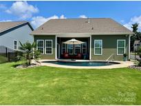Backyard pool with an umbrella and lounge furniture surrounded by a green lawn and privacy fence at 1638 Sweetmoss Loop, Denver, NC 28037