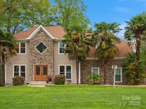 Charming home featuring stone accents, a manicured lawn, and mature landscaping with palm trees at 9009 Stourbridge Dr, Huntersville, NC 28078