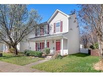 Charming two-story home with red shutters and a welcoming front porch surrounded by lush greenery and blooming trees at 12419 Swan Wings Pl, Huntersville, NC 28078