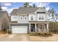 Charming two-story home featuring a stone facade, covered porch with rocking chairs and a two car garage at 1004 Whipcord Dr, Waxhaw, NC 28173