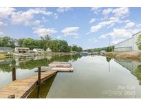 Scenic waterfront view featuring a private dock, calm water, and lush green trees under a partly cloudy blue sky at 7790 Blackwood Rd, Denver, NC 28037