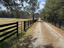 A long gravel driveway, lined with a black wooden fence, leads to a secluded property surrounded by trees and pasture at 18637 Davidson Concord Rd, Davidson, NC 28036