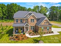 Beautiful brick home featuring lush landscaping, a welcoming front porch, and mature trees at 8601 Balcony Bridge Rd, Huntersville, NC 28078
