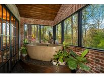 Bathroom with a standalone tub, brick accent wall, and lots of plants offering a spa-like and serene atmosphere at 4313 Kingswood Rd, Charlotte, NC 28226