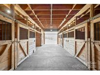 A rustic barn interior featuring wooden stalls and a concrete floor, providing a functional and charming equestrian facility at 447 Willow Pond Ln, Hiddenite, NC 28636