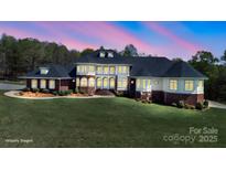 A stunning exterior shot of a large home with a manicured lawn, brick accents, and many windows glowing in the evening light at 447 Willow Pond Ln, Hiddenite, NC 28636