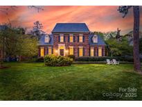 Stately brick home with manicured lawn and two chairs on the front lawn at sunset at 7700 Red Oak Ln, Charlotte, NC 28226