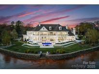 Expansive waterfront estate features a private pool, lush landscaping, and stunning architectural details at sunset at 8228 Bay Pointe Dr, Denver, NC 28037