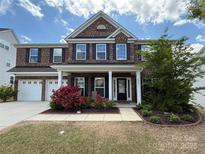 Charming two-story brick home with a manicured lawn, a two-car garage and a covered front porch at 9937 Travertine Trl, Davidson, NC 28036