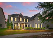 Charming two-story home with stone accents, covered porch, manicured landscaping and illuminated by accent lights at twilight at 11523 Warfield Ave, Huntersville, NC 28078