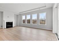 Bright, neutral living room featuring a fireplace, hardwood floors, and large windows offering natural light and treetop views at 3050 Tramore Dr, Harrisburg, NC 28075