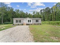 Charming single-story home with gray siding, black shutters, and a gravel driveway surrounded by lush greenery at 253 Artemis Pl # 27, Kershaw, SC 29067