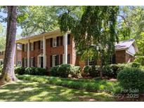 Charming two-story brick home with white columns, lush landscaping, and mature trees on a sunny day at 5510 Sardis Rd, Charlotte, NC 28270