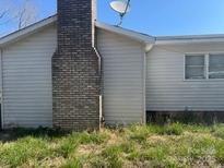 Side exterior view of home showcasing brick chimney, satellite dish, and vinyl siding at 143 Harvest Dr, Kings Mountain, NC 28086