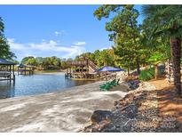 A tranquil beach with a private pier, blue umbrella, and seating offers a serene waterfront experience at 18420 Rosapenny Rd, Charlotte, NC 28278