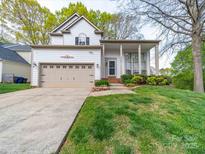 Traditional home featuring a manicured lawn, a beige garage door, and a charming front porch at 12708 Hollyhock Ln, Huntersville, NC 28078