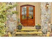 Elegant wooden front door with glass panels surrounded by stone and potted plants at 19040 Mary Ardrey Cir, Cornelius, NC 28031