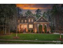 Dusk view of a charming brick two-story home with landscaped yard and warm exterior lighting at 10823 Preservation Park Dr, Charlotte, NC 28214