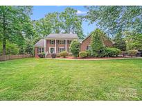 Traditional two-story brick home with a lush green lawn and mature trees providing ample shade at 6730 Gold Wagon Ln, Mint Hill, NC 28227