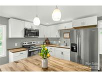 Bright kitchen features white cabinets, stainless steel appliances, and butcher block countertops, illuminated by pendant lighting at 212 W Doc Garris Rd, Lancaster, SC 29720