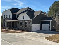 Beautiful two-story home featuring a three-car garage, stone accents, dark siding, and white trim under a brilliant blue sky at 7001 New Town Rd, Waxhaw, NC 28173