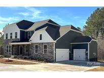 Beautiful two-story home featuring stone accents, a covered porch, attached three-car garage, and a manicured lawn at 7001 New Town Rd, Waxhaw, NC 28173