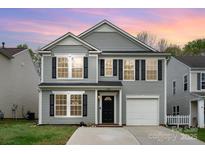 Charming two-story home with gray siding, black shutters, a well-kept lawn, and attached garage at sunset at 2005 Dunsmore Ln, Waxhaw, NC 28173