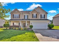 Charming two-story home featuring a manicured lawn and welcoming front porch with beautiful landscaping at 6115 The Meadows Ln, Harrisburg, NC 28075